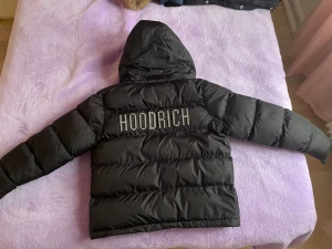 Svart pufferjacka från Hoodrich M(10-12år) - Svart pufferjacka från Hoodrich med stor logga på ryggen och mindre logga på bröstet. Jackan har huva, dragkedja framtill och är vadderad för extra värme. Perfekt för kalla dagar och riktigt snygg streetstil. Använd bara 1 gång  som nytt! Köpte för 1199 säljer bara 650