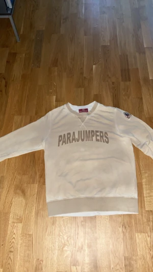 Beige fleece-tröja från Parajumpers - Säljer en beige fleece-tröja från Parajumpers i storlek L. Tröjan har lång ärm, rund hals och stort Parajumpers-tryck på bröstet. På ena ärmen finns ett snyggt broderat märke. Materialet är mjuk fleece och muddar vid ärmslut och nederkant ger extra komfort.  ANVÄND ENDAST ETT FÅTAL GÅNGER!!!