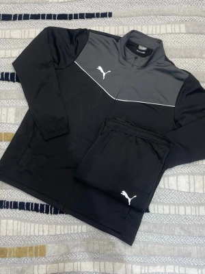 Adidas Träningsset - *   🎨 Färg: Grå, Svart *   📏 Storlek: XL *   🧶 Mönster: Grå, svart fin design *   🧵 Detaljer: Puma logga vid brösten, byxorna har zip vid benen så man kan öppna upp de lite. *   💃 Stil: Casual, Sportig *   ☀️, 🍂, ❄️, 🌷 Säsong: Alla säsonger *   👕 Passform: Sportig *   📝 Ytterligare beskrivningar: Fin set som passar perfekt för träning. *   ♻️ Skick: Helt ny *   🔎 Nyckelord: Träning, sportig, puma   Lägg till i paket för att spara upp till 20%!  För frågor eller erbjudanden, skicka ett meddelande!