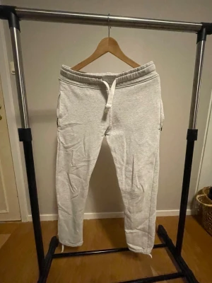 Russe Merch Mjukisbyxor - Ljusgrå mjukisbyxor från R i storlek XS. Byxorna har resår i midjan med snörning och raka ben. Perfekta för chill dagar eller när du vill vara extra bekväm. Mjukt material och neutralt utseende som passar till det mesta.