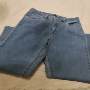 Blå jeans från Mingel, raka ben - Klassiska blå jeans från Mingel i rak modell med normal passform. Jeansen har fem fickor, bälteshällor och stängs med knapp och dragkedja. Snygga sömdetaljer på bakfickorna och tillverkade i slitstarkt denimtyg.
