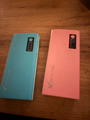 Arctic Tern Powerbank D566 13000mAh - Två Arctic Tern powerbanks, modell D566, med kapacitet på 13000mAh. Utrustade med två USB-portar (5V/2.1A) och batteriindikator. Färger: blå och rosa. Mindre ytslitage syns, men i gott skick och perfekt för att ladda mobilen på språng.