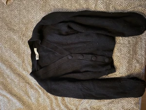 Svart ribbad kofta från Zara - Svart ribbad kofta från Zara med v-ringning och stora knappar framtill. Långärmad och i mjukt stickat material som ger en skön och stilren look. Perfekt att slänga över en topp eller klänning för en chill vibe.