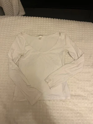 Vit långärmad basic topp  - Säljer en enkel och stilren vit långärmad topp med djup rundad ringning. Toppen är i mjuk bomull och har en slim passform som sitter snyggt på kroppen. 