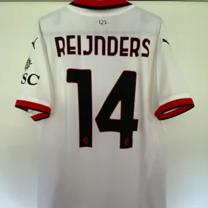 AC Milan Reijnders 14 bortatröja Puma - AC Milan bortatröja med Reijnders och nummer 14 på ryggen. Vit med svarta och röda detaljer, svart Puma-logga och klubbmärke på bröstet. Kortärmad modell i lätt och ventilerande polyester. Klassisk krage med röd och svart rand. Snygg och sportig design.