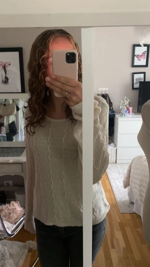 Beige stickad tröja med vågigt mönster, från vila - Säljer en beige stickad tröja med vågiga detaljer framtill. Tröjan har rund hals och långa ärmar, perfekt för dig som gillar en enkel men snygg look. Passar till jeans eller kjol och är supermjuk mot huden.