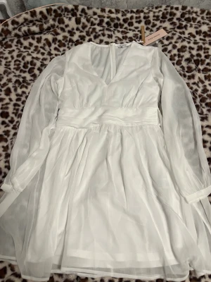 Vit omlottklänning från Bubbleroom - Superfin vit kortklänning från Bubbleroom med v-ringning, långa transparenta ärmar och knytband i midjan. Helt oanvänd. Klänningen har ett flowy fall och markerad midja, perfekt för dig som gillar en romantisk och stilren look.