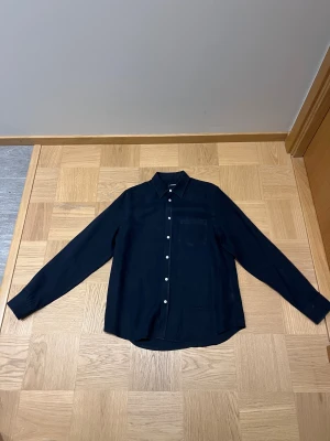 Marinblå linneskjorta från J.Lindeberg - Snygg marinblå skjorta från J.Lindeberg i mjukt linne. Riktigt schysst nästan i nyskick. Ända defekten är en liten solfläck vid revbenen. Utöver det riktigt fin. Storleken är M