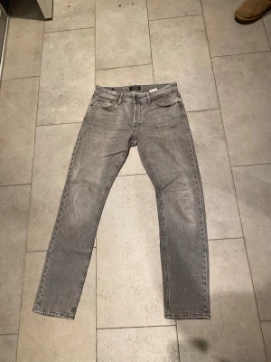 Grå jeans från Jack & Jones, 31/34 - Säljer ett par grå jeans från Jack & Jones i storlek 31/34. Jeansen har klassisk femficksdesign, raka ben och normal passform. Snygg tvättad grå färg som passar till det mesta. Perfekta för dig som gillar stilrena och enkla jeans.