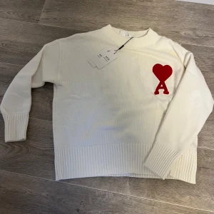 Vit stickad tröja från Ami Paris - Snygg vit stickad tröja från Ami Paris med röd hjärtlogga påse och allt följs med säljer för den var för liten är 175cm lång 