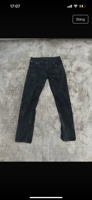 Svarta jeans från Nudie Jeans, 30/32 - Snygga svarta jeans från Nudie Jeans i klassisk femficksmodell. Jeansen har en rak passform och är tillverkade i slitstark bomull med Nudie Jeans logga på bakfickan och läderpatch i midjan. Perfekt för dig som gillar stilrena och tidlösa jeans.