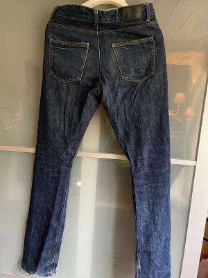Mörkblå jeans från Whyred, 29/32 - Snygga mörkblå jeans från Whyred med klassisk femficksdesign och raka ben. Jeansen har kontrastsömmar och en stilren svart läderpatch med Whyred-logga bak i midjan. Perfekt passform och tidlös look för dig som gillar stilrena jeans.
