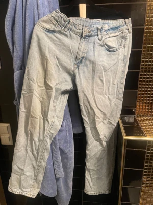 Ljusblå tapered jeans från H&M - Säljer ett par ljusblå jeans från H&M med relaxed passform och justerbar midja. Modellen har tapered ben och klassiska fem fickor. Jeansen är tillverkade i bomull och har en snygg, avslappnad vibe som passar perfekt till sneakers. Har inte avänds på länge därför är de skrynkliga.
