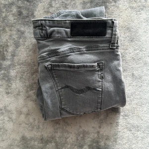 Grå slim jeans med svarta detaljer - Snygga grå jeans med slim passform och svarta detaljer på bakfickan samt svart patch vid linningen. Klassisk femficksmodell och raka ben. Perfekta till vardags för en stilren look.