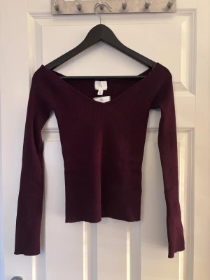 Vinröd ribbad topp från H&M - Säljer en vinröd ribbad topp från H&M i storlek S. Toppen har lång ärm, djup v-ringning och är figurnära i modellen. Materialet är mjukt och stretchigt, perfekt för dig som gillar en slim passform och stilren look.