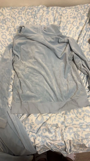 Ljusblå velour hoodie Juicy Couture - Säljer en ljusblå hoodie från Juicy Couture i mjuk velour med dragkedja och huva. Tröjan har långa ärmar, fickor fram och en snygg J-detalj på dragkedjan. Perfekt för dig som gillar den klassiska Y2K-stilen och vill ha något riktigt comfy.