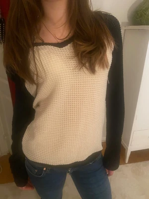 Offshoulder stickad tröja svart/beige - Snygg offshoulder stickad tröja i beige med svarta kontrastärmar och svarta kanter. Tröjan har en v-ringad hals och långärmade ärmar. Mjuk och skön struktur som ger en cool vibe till din outfit. Perfekt för dig som gillar att sticka ut lite extra.