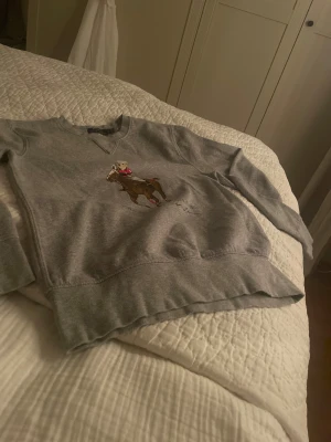 Grå sweatshirt Polo Ralph Lauren XS - Säljer en grå sweatshirt från Polo Ralph Lauren i storlek XS. Tröjan har ett stort tryck med Polo Bear som spelar polo på häst, och texten 'POLO BEAR BY RALPH LAUREN' under motivet. Mjuk insida och klassisk rund hals. Perfekt för dig som gillar sportiga och stilrena plagg. Den e perfekt för en mysig kväll i sommaren och alla högtider😁😁 (säljer pga ska köpa julklappar till mina föräldrar) pris kan diskuteras.