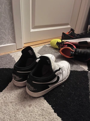 Nike Air Jordan 1 Low svart/vit - Nike Air Jordan 1 Low sneakers i svart och vitt med klassisk rund tå och perforerad ovandel. Skorna har snörning, svart swoosh på sidan och Jordan-logga på hälen. Tillverkade i skinn med platt sula och låg profil. Perfekt för dig som gillar streetwear och ikoniska sneakers.