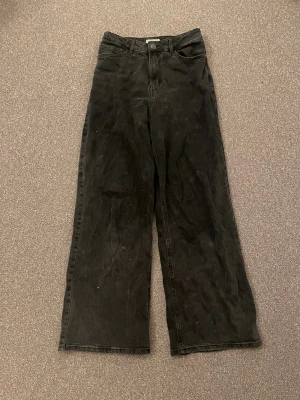 Svarta baggy jeans från Lindex - Säljer ett par svarta jeans från Lindex med hög midja och breda ben. Klassisk femficksmodell med bälteshällor och knappgylf. Jeansen är i ett mjukt bomullsmaterial och har en riktigt chill och avslappnad vibe. Rekommenderas starkt!