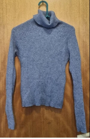 Blå ribbad polotröja - Mysig blå polotröja med ribbat mönster och lång ärm. Tröjan har en hög polokrage och är stickad i ett mjukt material som passar perfekt när det är kallt ute. Enkel och stilren design som är lätt att matcha med olika outfits.