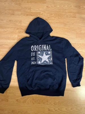Scndi hoodie - Snygg mörkblå hoodie från scndi med stort tryck framtill som har stjärnor⭐️och texten 'Original Fit Est. 2024'. Tröjan har huva, magficka och långa ärmar. Perfekt för dig som gillar coola detaljer.