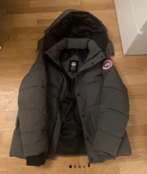 Mörkgrå Canada Goose dunjacka med päls - Säljer en mörkgrå dunjacka från Canada Goose med avtagbar huva och pälsdetalj. Jackan har klassisk patch på ärmen, dragkedja och knappar framtill samt ribbade muddar. Perfekt för kalla dagar och har en schysst oversized look.