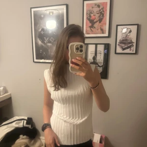 Vit ribbad ärmlös topp från Zara - Säljer en snygg vit topp från Zara med ribbad struktur och ärmlös design. Toppen har en rund halsringning och är gjord i ett mjukt syntetmaterial som sitter skönt mot kroppen. Perfekt för dig som gillar stilrena och enkla plagg med lite edge.