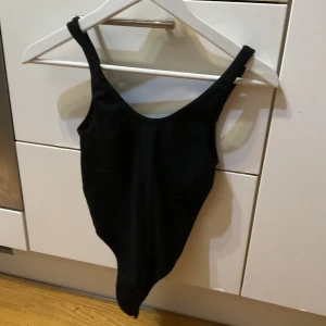 Svart ärmlös bodysuit - Säljer en svart, tight bodysuit med djup urringning och breda axelband. Den är ärmlös och har en klassisk, stilren look som passar perfekt till jeans eller kjol. Materialet känns mjukt och stretchigt för en bekväm passform. Från skims blivit för liten för mig 
