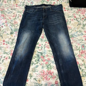 Emporio Armani blå jeans - Snygga blå jeans från Emporio Armani med klassisk femficksdesign och diskret logga på bakfickan. Jeansen har en slimfit passform, slitningar och ljusare prickar fram och bak.       W34 L32. Främre fickorna har hål i sig, behöver sys för att bli bra. Inga små hål utan fickorna inne är ganska öppna. 