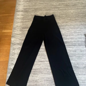 Svarta vida byxor med hög midja - Snygga svarta byxor med hög midja och vida ben. Perfekta för en clean och stilren look. Byxorna har en enkel design utan synliga detaljer och är gjorda i ett mjukt, följsamt tyg som ger en skön passform.