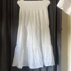 Vit sommarkjol från Gina Tricot - Säljer en vit kjol från Gina Tricot i storlek 158/164. Kjol är lång, har smock upptill och är sydd i 100% bomull med broderade små blommor över hela tyget. Perfekt för varma dagar och har en luftig, flowy passform.