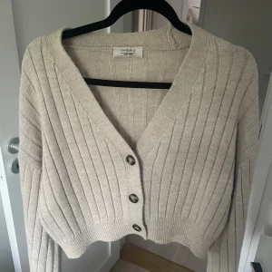 Beige ribbad cardigan  - Superfin beige cardigan från Chiquelle med ribbat stickat material och v-ringning. Koftan har tre stora knappar framtill med långa ärmar. Perfekt att slänga över en topp för en chill look. Strl ONE SIZE💓