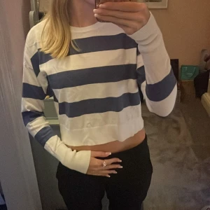 Randig croppad tröja  - Säljer en croppad långärmad tröja med breda marinblå och vita ränder. Tröjan har normal passform, rund halsringning och är tillverkad i mjuk bomull. 