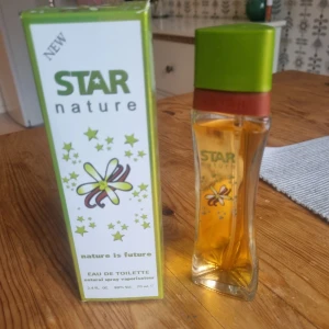 Star Nature Eau de Toilette 70ml - Fräsch parfym från Star Nature med grön och vit förpackning dekorerad med stjärnor och blommor. Flaskan är smal och genomskinlig med grönt lock och röd detalj, innehåller 70 ml doft. Perfekt för dig som gillar naturliga och fräscha toner.