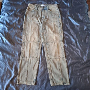 Gråaktiga jeans från ASOS Design - Säljer ett par gråa jeans från ASOS Design med raka ben och stora detaljer framtill. Byxorna är tillverkade i jeansmaterial och har klassisk midja med bälteshällor. Perfekta för en avslappnad och trendig look.