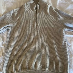 Beige ribbad stickad tröja half zip - Beige stickad tröja med ribbad struktur och hög krage. Tröjan har en half zip-dragkedja framtill och långa ärmar. Perfekt för lager-på-lager och chill höst- och vinterdagar.