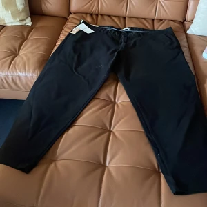 Svarta kostymbyxor med rak passform - Stilrena svarta kostymbyxor med rak passform och klassisk design. Byxorna har diskreta fickor och midja med hällor för bälte. Perfekta för en clean och snygg look. Materialet känns mjukt och följsamt.