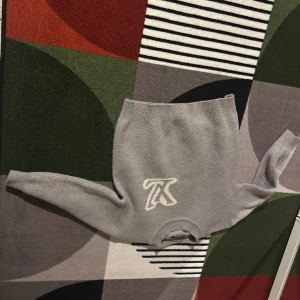 Grå stickad tröja från Louis Vuitton - Säljer en grå stickad tröja från Louis Vuitton med ett stort vitt LV-logotypbroderi framtill. Tröjan har rund halsringning och långa ärmar, perfekt för dig som vill ha en stilren och exklusiv look.