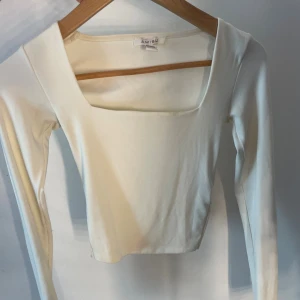 Vit långärmad topp från Amisu - Säljer en stilren vit långärmad topp från Amisu med fyrkantig urringning. Toppen är croppad och har en clean, minimalistisk look som passar perfekt till jeans eller kjol. Tillverkad i mjukt material som känns skönt mot huden.