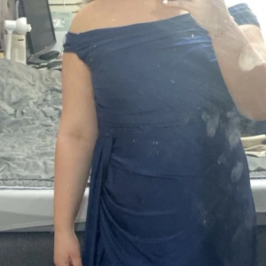 Marinblå långklänning offshoulder - Säljer en marinblå långklänning med offshoulder-modell och draperade detaljer. Klänningen har en elegant slits på sidan och är figurnära upptill. Perfekt för dig som vill ha en stilren och klassisk look. Använd endast i två tillfällen i ett par timmar. 