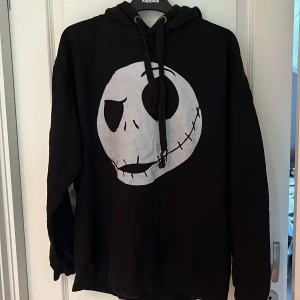 Svart hoodie med Jack Skellington-tryck - Svart hoodie med stor vit Jack Skellington-tryck på framsidan, inspirerad av The Nightmare Before Christmas. Tröjan har huva med snörning och långa ärmar. Perfekt för dig som gillar film och vill sticka ut med en cool look.