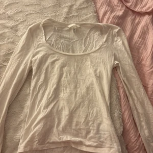 Vit långärmad tröja från H&M - En enkel och stilren vit långärmad tröja från H&M i storlek S. Tröjan har en rundad halsringning och är gjord i mjuk bomull, perfekt för layering eller att bära som den är. Passformen är normal och materialet känns lätt mot huden.