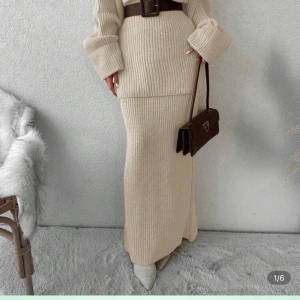Beige stickad långkjol med matchande tröja  - Snygg och mysig höst-/vinterlook med beige stickad tröja och beige stickad långkjol. Tröjan har rund hals, lång ärm och en loose passform med grovstickad struktur som ger en avslappnad, chill vibe. Kjolen har rak passform, bred resår i midjan och ribbstickning med mjuk, chunky känsla – perfekt för kalla dagar. Tillsammans skapar de en harmonisk, trendig outfit som är enkel att styla med boots eller sneakers för både vardag och lite uppklädda tillfällen.