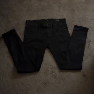 Replay Anbass svarta jeans, stl 32 - Svarta Replay Anbass jeans i slim fit med klassisk femficksdesign och snyggt smal passform. Jeansen har en stilren look och är gjorda i mjukt stretchigt material för extra komfort. Perfekta för dig som gillar en modern och clean stil.