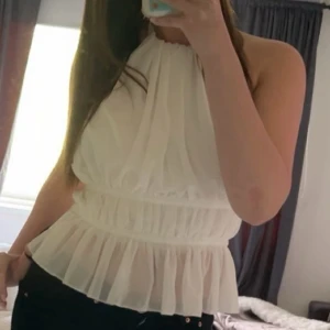 Vit omlott blus med knytband - Säljer en superfin vit blus i omlottmodell med volangkant nertill. Toppen har halterneck och knytning i ryggen, vilket ger en öppen rygg och snygg passform. Perfekt till jeans eller kjol för en fräsch look. Materialet är lätt och luftigt.