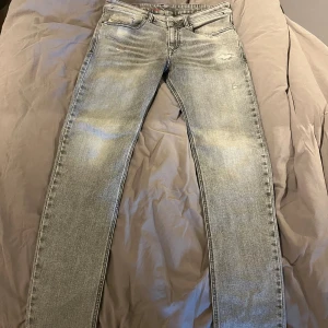 Grå slitna jeans från Diesel - Säljer ett par grå jeans från Diesel med snygga slitningar och en tvättad look. Jeansen har rak/skinny passform och klassisk femficksdesign. Perfekta för dig som gillar en avslappnad och trendig stil. Näst intill aldrig använda, köpt från Zalando. Storlek w30,l30