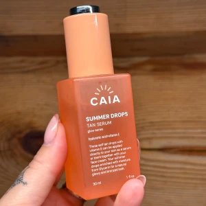 CAIA Summer Drops Tan Serum - Glow-serum i snygg orange glasflaska med pump. Innehåller hyaluronsyra och vitamin E för återfuktning och lyster. Perfekt för att få en solkysst look året runt. Kan blandas med ansiktskräm eller användas direkt på huden.
