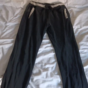 Svarta mjukisbyxor från EA7 Armani - Svarta mjukisbyxor från EA7 Emporio Armani med kontrastfärgade detaljer vid midjan och fickorna. Byxorna har två bakfickor, elastisk midja och är tillverkade i 100% bomull. Perfekta för en chill och sportig look.