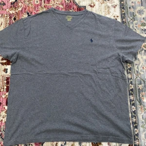 Grå v-ringad t-shirt Polo Ralph Lauren - Snygg grå t-shirt från Polo Ralph Lauren med klassisk v-ringning och broderad marinblå logga på bröstet. Modellen är kortärmad och har en normal passform. Perfekt för dig som gillar stilrena och enkla plagg med en touch av premiumkänsla.